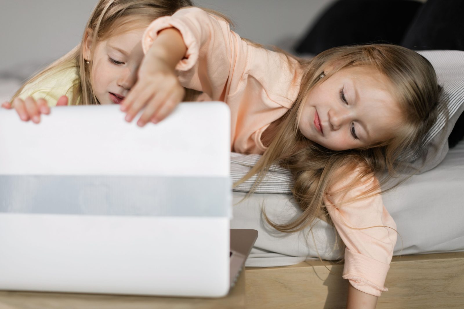 Două fetițe întinse pe un pat, lângă un laptop