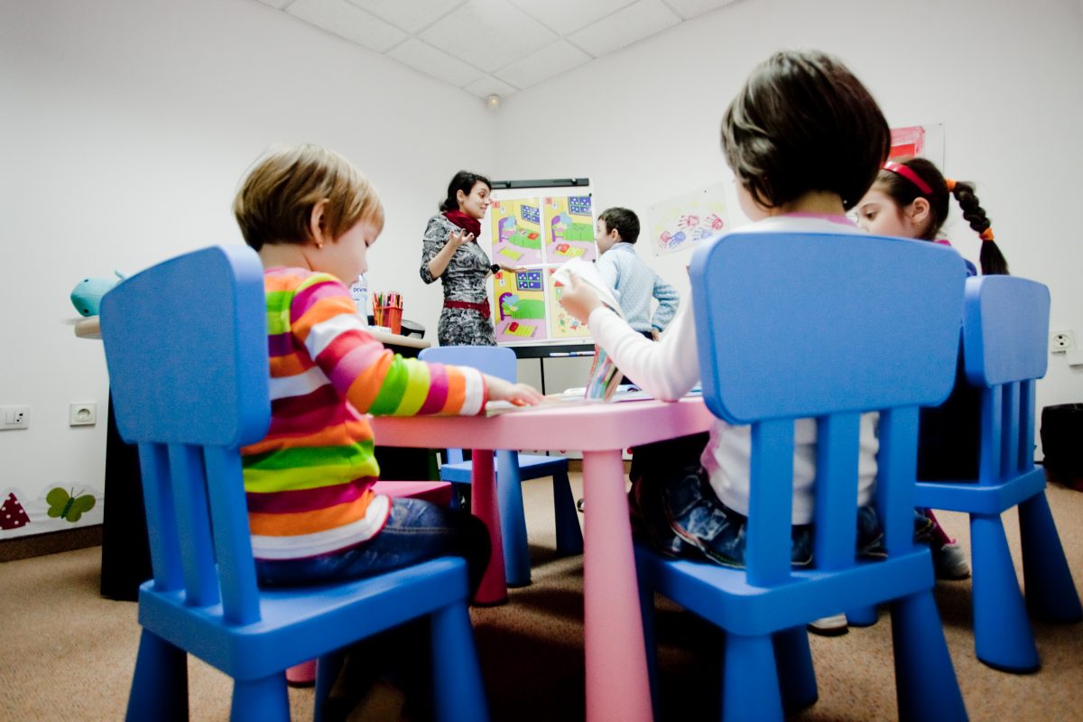 Copii la o masă de lucru în sala Echo Kids, cu profesoara la flipchart